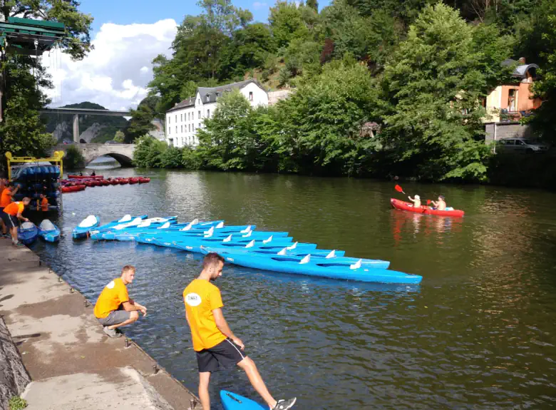 Kayaks alignés sur la Lesse à l&rsquo;arrivée à Anseremme, pont de pierre et viaduc de Dinant en arrière-plan