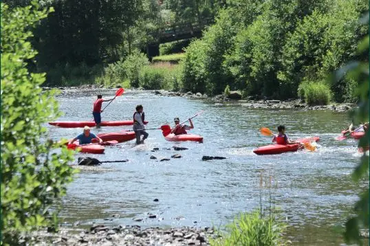 Groupe de kayaks rouges sur une rivière ardennaise peu profonde, devant un pont et une berge boisée